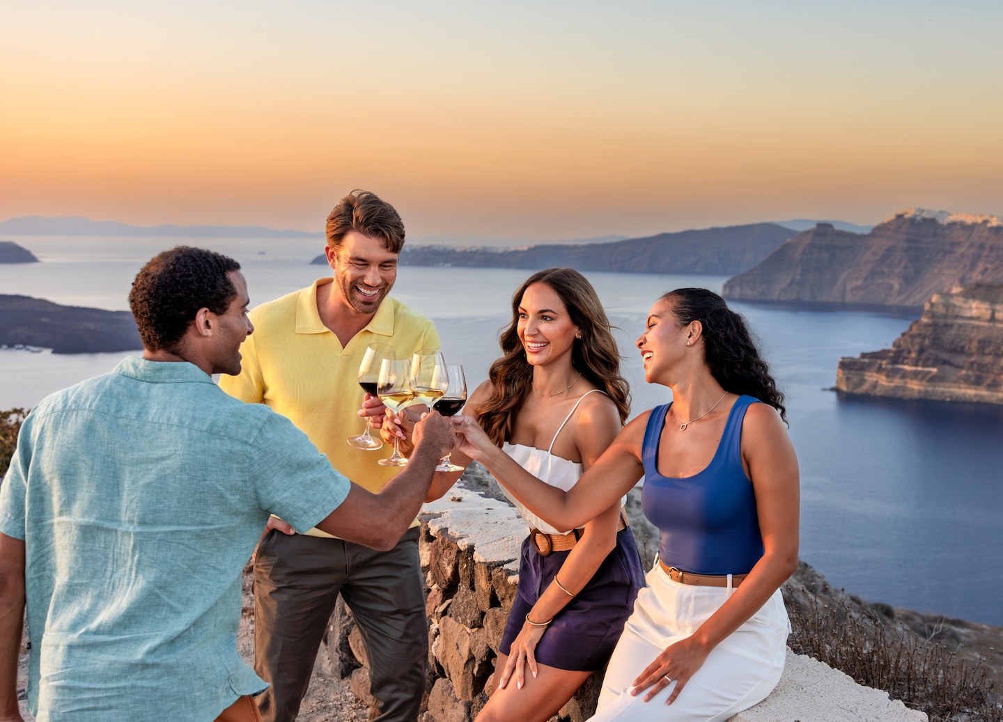 Friends toast crisp Santorini wine overlooking Megalochori’s sunlit volcanic cliffs. - Santorini, Greece