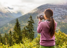 outdoor travel lifestyle woman photographer shooting video camera at alaska background usa