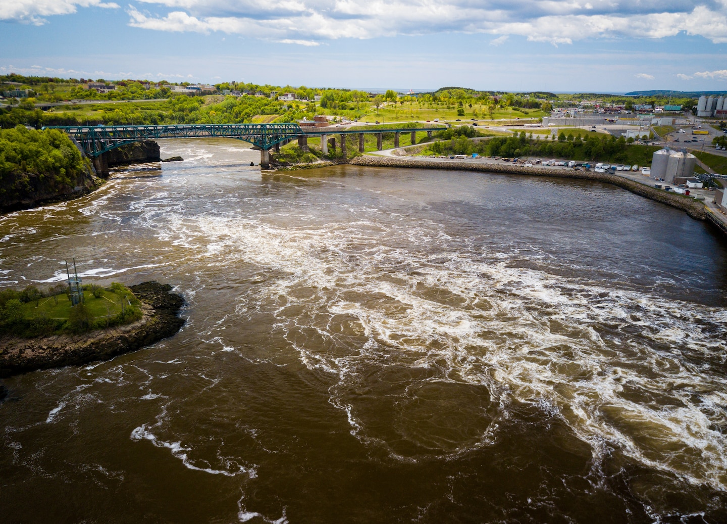 River rapids rush beneath a small bridge, surrounded by rocky banks and forested greenery. - Saint John (Bay of Fundy), New Brunswick
