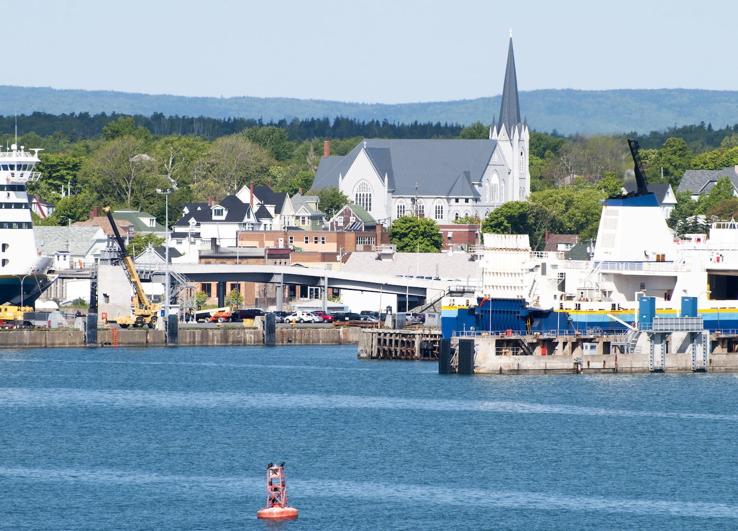 Sydney’s harbor dock shows wooden piers, calm coastal water, and distant shoreline buildings under clear skies. - Sydney, Nova Scotia