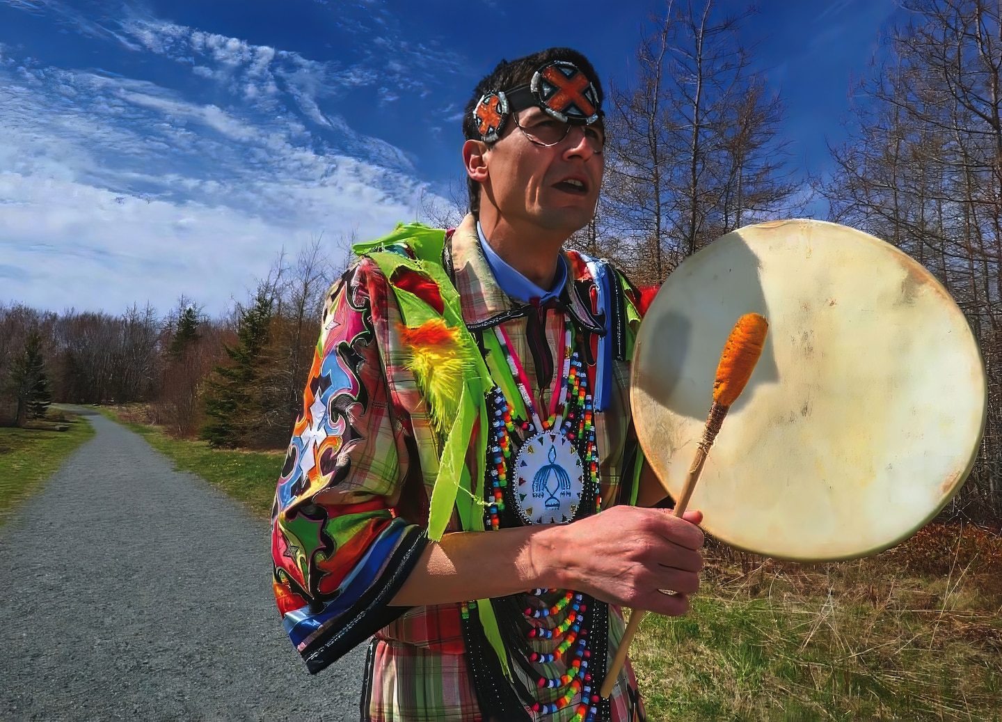 A Mi’kmaw man plays a hand drum outdoors, sharing traditional music during a cultural experience. - Sydney, Nova Scotia